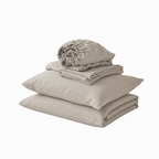 A stack of folded beige bedding, including a pillowcase, sheet, and a rolled fabric piece, displayed on a white bed in a softly lit bedroom setting.